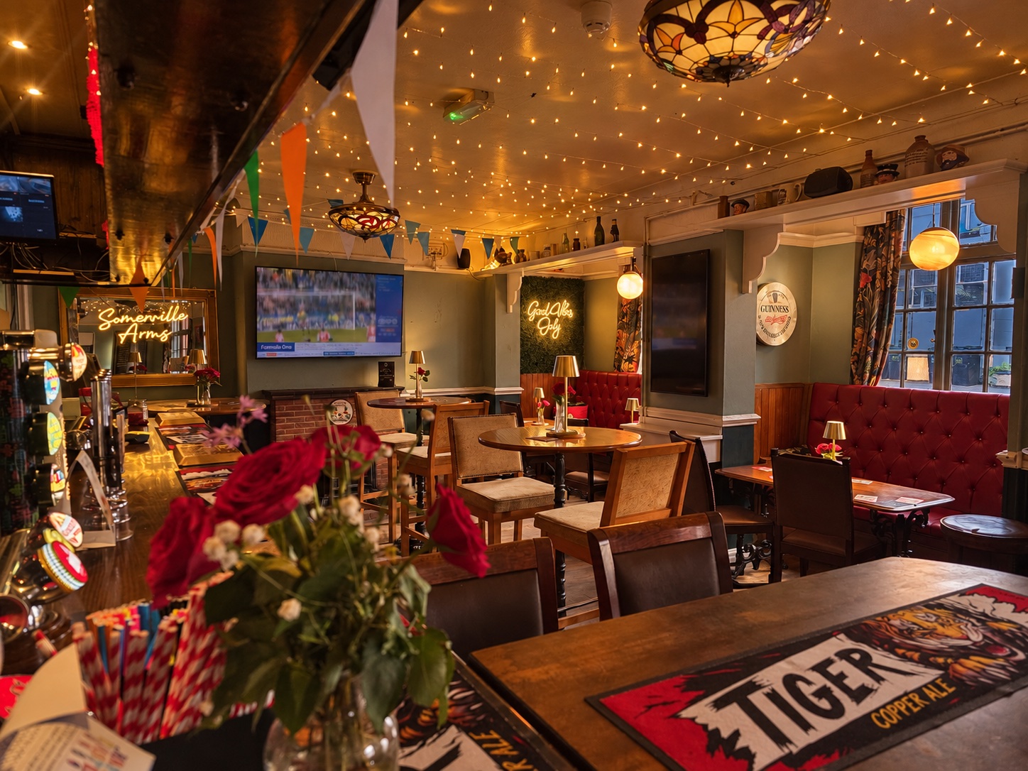 The warmly lit bar with wooden tables, red seating and strings of lights